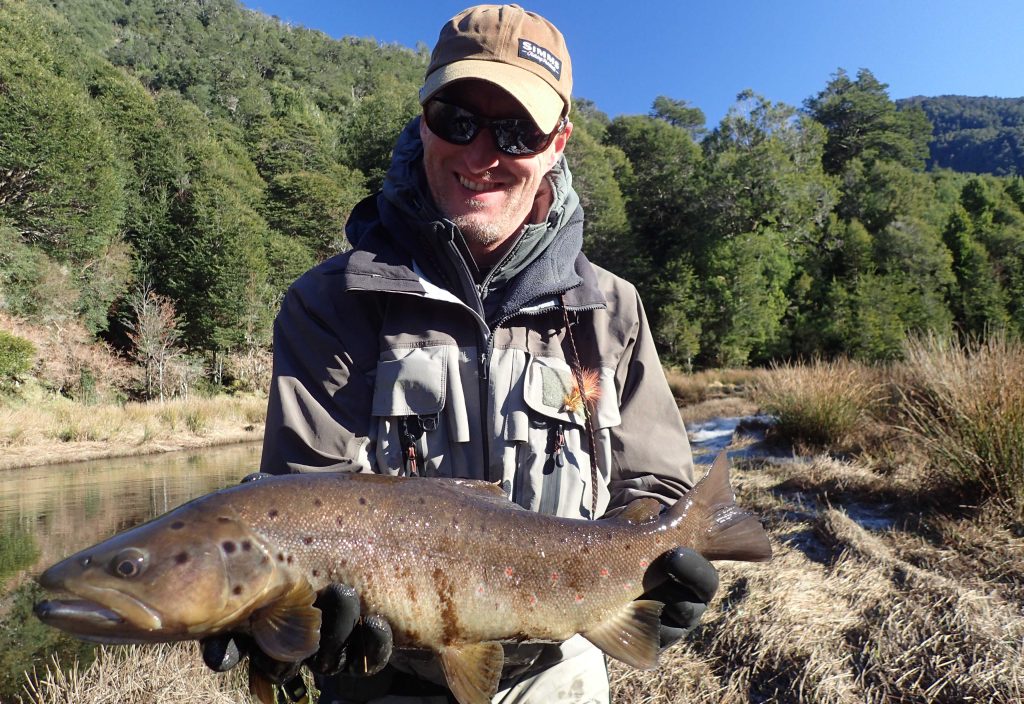 Guide Andi Manstein kneeling on the riverbank with a large brown trout