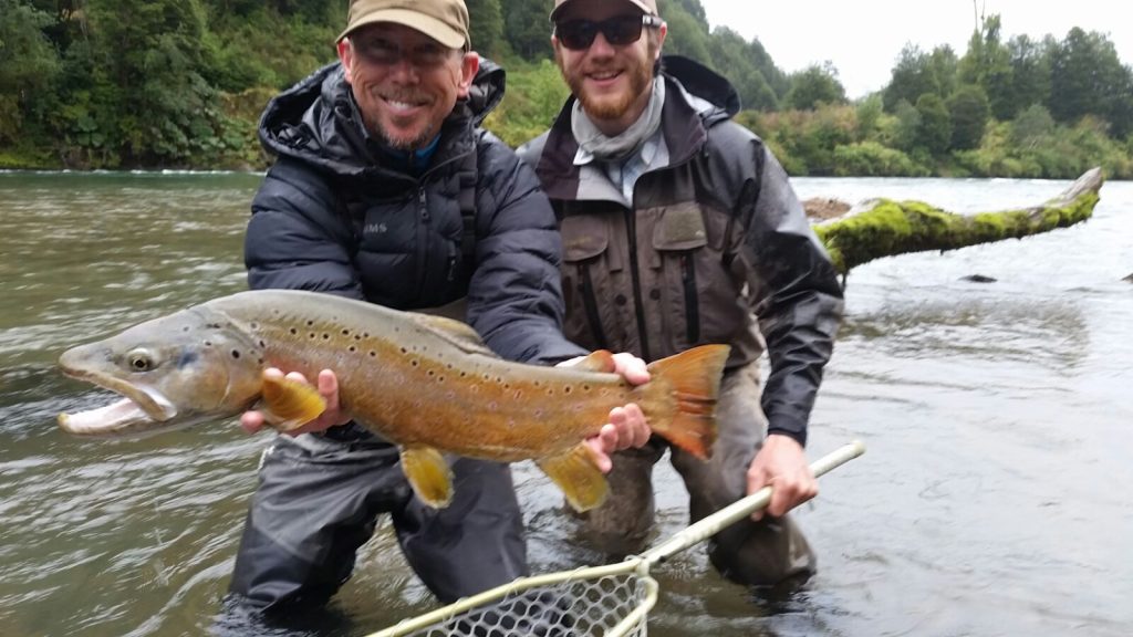 Guide Ben Kittell and an angler wading the river with a brown trout and landing net